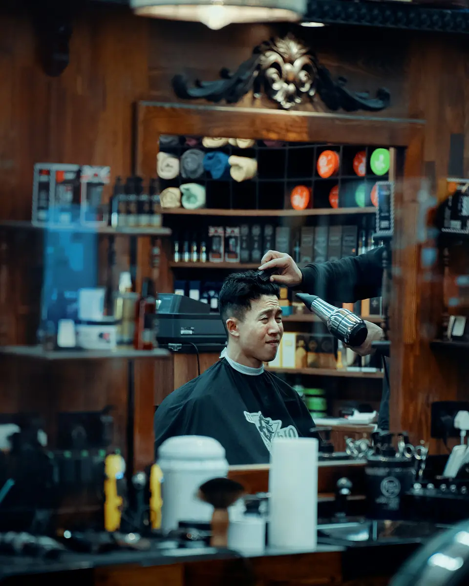 Barber mengeringkan rambut pelanggan di barbershop berdinding kayu