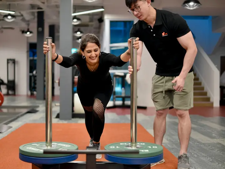 Personal trainer mendampingi kliennya latihan di gym